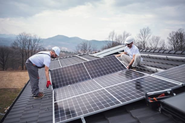 Caucasian men installing panels on a house roof.