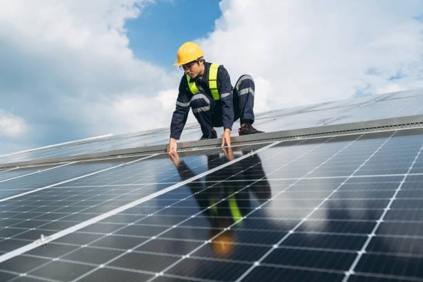 A service engineer checks a solar cell that is mounted on the roof to see if there is a damaged component that needs to be repaired. Concept of energy from natural sources.